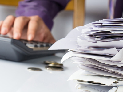 Person using calculator next to stack of papers with coins on table